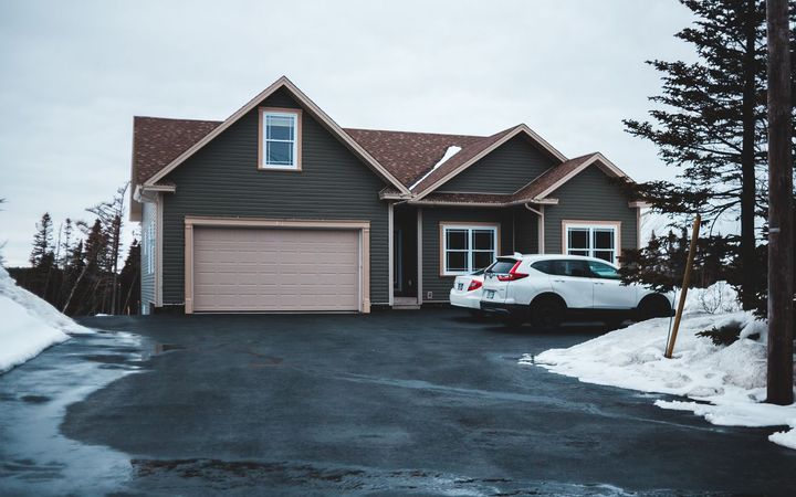 Wide blacktop driveway in front of a gray house, with snow along the edges