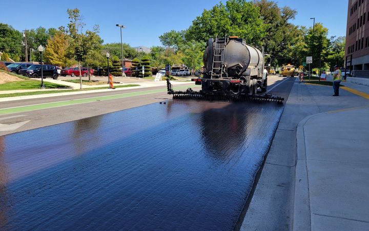 Distributor truck spraying a glossy black coat over a street