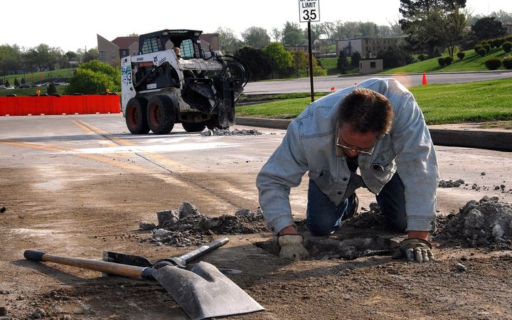 Worker kneeling to fill a pothole with fresh asphalt
